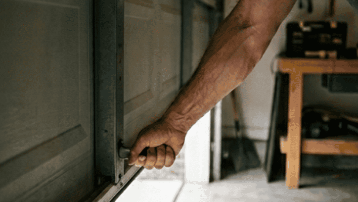Homeowner lifting heavy garage door manually because of failing garage door spring
